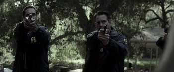 Movie still from “The Veil” (2016), directed by Phil Joanou – A man holding a gun while standing in front of a tree; Medium shot, Over the shoulder angle