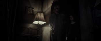 Movie still from “The Veil” (2016), directed by Phil Joanou – A man standing next to a lamp in a dark room; Wide shot, Low angle