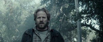 Movie still from “The Veil” (2016), directed by Phil Joanou – A man standing in front of a tree with trees in the background; Close Up shot, Low angle