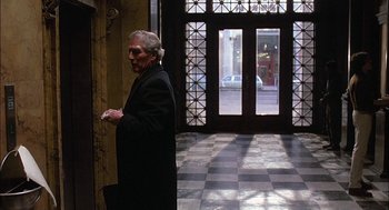 Movie still from “The Verdict” (1982), directed by Sidney Lumet – An older man in a black coat walking in a lobby; Wide shot, Over the shoulder angle