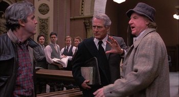 Movie still from “The Verdict” (1982), directed by Sidney Lumet – Two men in suits talking to each other in front of a crowd; Medium shot, Over the shoulder angle