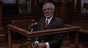 Movie still from “The Verdict” (1982), directed by Sidney Lumet – An older man wearing a suit and tie sitting at a podium; Medium shot, High angle