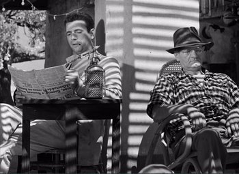 Movie still from “The Wages of Fear” (1953), directed by Henri-Georges Clouzot – A man sitting next to another man reading a newspaper; Medium shot, High angle