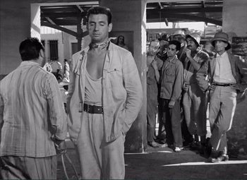 Movie still from “The Wages of Fear” (1953), directed by Henri-Georges Clouzot – Black and white photograph of a man in front of a group of men; Medium shot, Low angle