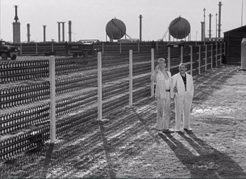 Movie still from “The Wages of Fear” (1953), directed by Henri-Georges Clouzot – Two men standing next to each other in front of a fence; Wide shot, Low angle