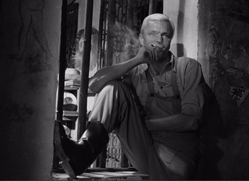 Movie still from “The Wages of Fear” (1953), directed by Henri-Georges Clouzot – An older man smoking a cigarette while leaning against a wall; Medium shot, Low angle