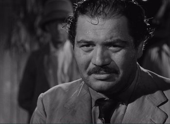 Movie still from “The Wages of Fear” (1953), directed by Henri-Georges Clouzot – A man in a suit and tie looking at the camera; Close Up shot, Over the shoulder angle