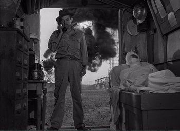 Movie still from “The Wages of Fear” (1953), directed by Henri-Georges Clouzot – A man standing in front of a window with smoke coming out of the window; Medium shot, Over the shoulder angle