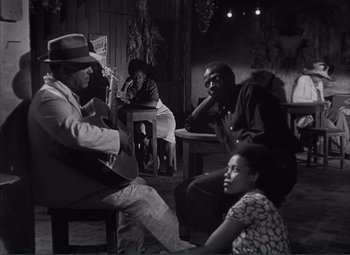 Movie still from “The Wages of Fear” (1953), directed by Henri-Georges Clouzot – A black and white photo of a group of people sitting around; Wide shot, Over the shoulder angle