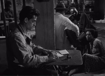 Movie still from “The Wages of Fear” (1953), directed by Henri-Georges Clouzot – Black and white photograph of a man writing at a table; Medium shot, High angle