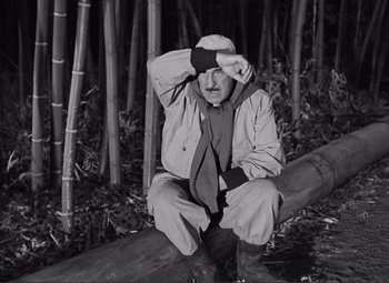 Movie still from “The Wages of Fear” (1953), directed by Henri-Georges Clouzot – An older man sitting on a log in the woods; Medium shot, High angle
