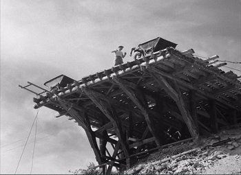 Movie still from “The Wages of Fear” (1953), directed by Henri-Georges Clouzot – A man standing on top of a wooden structure; Extreme Wide shot, Low angle