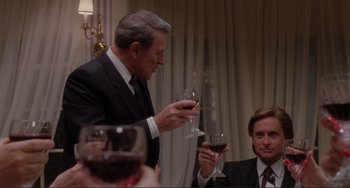 Movie still from “The War of the Roses” (1989), directed by Danny DeVito – A man in a suit and tie holding a wine glass; Medium shot, Over the shoulder angle