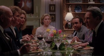 Movie still from “The War of the Roses” (1989), directed by Danny DeVito – A group of people sitting around a table with wine glasses; Medium shot, High angle