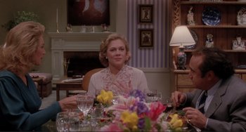 Movie still from “The War of the Roses” (1989), directed by Danny DeVito – A woman sitting at a dinner table with people around the table; Medium shot, Over the shoulder angle