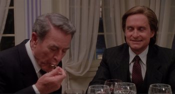Movie still from “The War of the Roses” (1989), directed by Danny DeVito – Two men sitting at a dinner table with wine glasses in front of them; Close Up shot, Over the shoulder angle