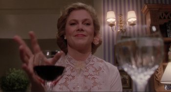 Movie still from “The War of the Roses” (1989), directed by Danny DeVito – A woman holding a glass of red wine in front of a mirror; Close Up shot, Low angle