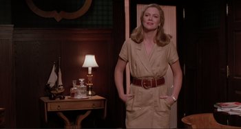 Movie still from “The War of the Roses” (1989), directed by Danny DeVito – A woman standing in front of a table with a lamp on it; Medium shot, Over the shoulder angle