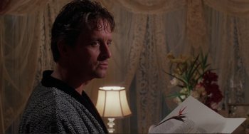 Movie still from “The War of the Roses” (1989), directed by Danny DeVito – A man standing next to a table with a lamp; Close Up shot, Low angle