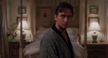 Movie still from “The War of the Roses” (1989), directed by Danny DeVito – A man standing in front of a bed in a room; Medium shot, Over the shoulder angle