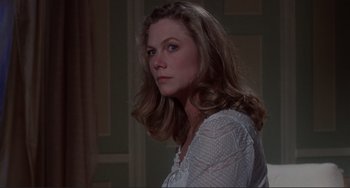 Movie still from “The War of the Roses” (1989), directed by Danny DeVito – A woman in a white shirt is standing in a room; Close Up shot, Over the shoulder angle