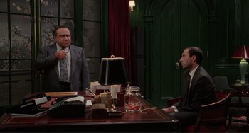 Movie still from “The War of the Roses” (1989), directed by Danny DeVito – Two men sitting at a table in front of each other; Medium shot, Over the shoulder angle