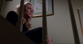 Movie still from “The War of the Roses” (1989), directed by Danny DeVito – A woman sitting on top of a stair rail; Medium shot, Low angle