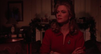 Movie still from “The War of the Roses” (1989), directed by Danny DeVito – A woman in a red shirt sitting in front of a fireplace; Close Up shot, Low angle