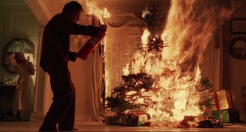Movie still from “The War of the Roses” (1989), directed by Danny DeVito – A man holding a fire extinguisher in front of a christmas tree on fire; Medium shot, Low angle