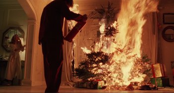 Movie still from “The War of the Roses” (1989), directed by Danny DeVito – A man holding a fire extinguisher in front of a christmas tree on fire; Medium shot, Low angle