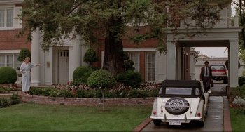 Movie still from “The War of the Roses” (1989), directed by Danny DeVito – A car is parked in front of a brick house; Wide shot, Low angle