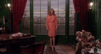 Movie still from “The War of the Roses” (1989), directed by Danny DeVito – A woman in a pink dress standing in front of a window; Wide shot, Over the shoulder angle