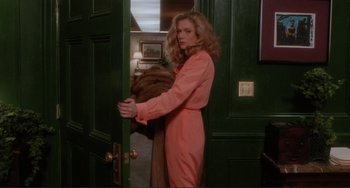 Movie still from “The War of the Roses” (1989), directed by Danny DeVito – A woman in a pink coat standing in front of a green door; Medium shot, Low angle