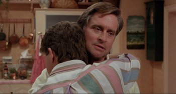 Movie still from “The War of the Roses” (1989), directed by Danny DeVito – A man hugging another man with his arms around another man; Close Up shot, Over the shoulder angle