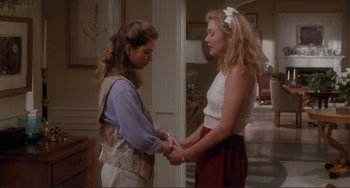 Movie still from “The War of the Roses” (1989), directed by Danny DeVito – Two young women holding hands while standing next to each other; Medium shot, Over the shoulder angle