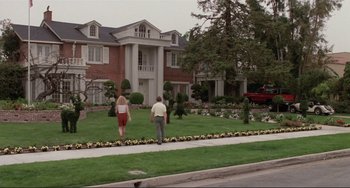 Movie still from “The War of the Roses” (1989), directed by Danny DeVito – Two people walking down a sidewalk in front of a house; Wide shot, Low angle