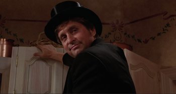 Movie still from “The War of the Roses” (1989), directed by Danny DeVito – A man wearing a black hat and a black suit; Close Up shot, Low angle
