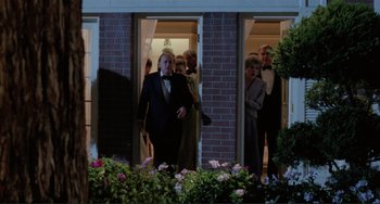 Movie still from “The War of the Roses” (1989), directed by Danny DeVito – A group of people standing in front of a building; Wide shot, Low angle