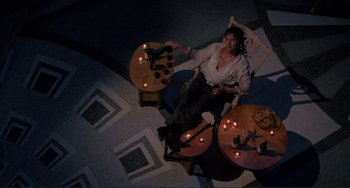 Movie still from “The War of the Roses” (1989), directed by Danny DeVito – A man sitting at a table with candles in a room; Wide shot, Overhead angle