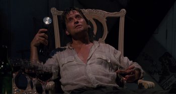 Movie still from “The War of the Roses” (1989), directed by Danny DeVito – A man sitting in a chair holding a glass of wine; Medium shot, Low angle