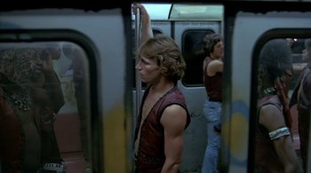 Movie still from “The Warriors” (1979), directed by Walter Hill – A man in a red shirt is standing on a subway train; Medium shot, Low angle