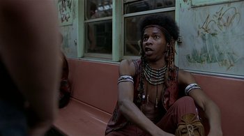 Movie still from “The Warriors” (1979), directed by Walter Hill – A man sitting on a bench with a lot of beads around his neck; Medium shot, Low angle