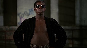 Movie still from “The Warriors” (1979), directed by Walter Hill – A man wearing a black jacket and sunglasses; Medium shot, Low angle