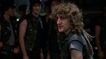 Movie still from “The Warriors” (1979), directed by Walter Hill – A man with long curly hair is looking to his left; Close Up shot, Over the shoulder angle