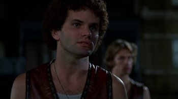 Movie still from “The Warriors” (1979), directed by Walter Hill – A man in a leather vest looks at the camera while another man stands in the background; Close Up shot, Low angle
