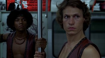 Movie still from “The Warriors” (1979), directed by Walter Hill – A man holding onto a metal pole while standing on a train; Close Up shot, Low angle