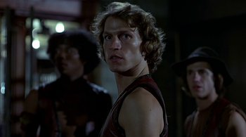 Movie still from “The Warriors” (1979), directed by Walter Hill – A young man with long blonde hair wearing a black shirt; Close Up shot, Low angle