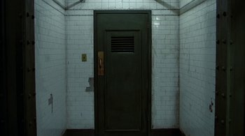 Movie still from “The Warriors” (1979), directed by Walter Hill – A green door in a room with white brick walls; Wide shot, High angle