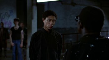 Movie still from “The Warriors” (1979), directed by Walter Hill – A man in a black shirt is talking to another man; Medium shot, Over the shoulder angle