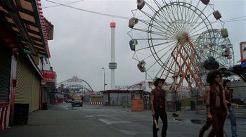 Movie still from “The Warriors” (1979), directed by Walter Hill – A man walking in front of a ferris wheel; Wide shot, High angle